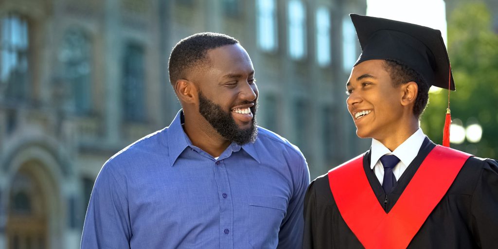 father smiling at son in graduation cap and gown