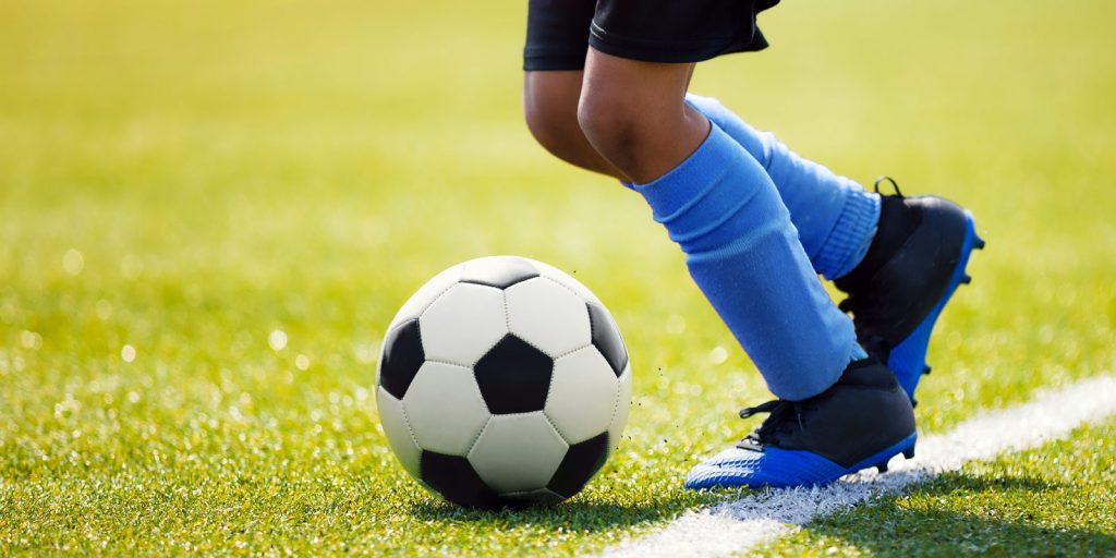 youth kicking soccer ball on field of green turf