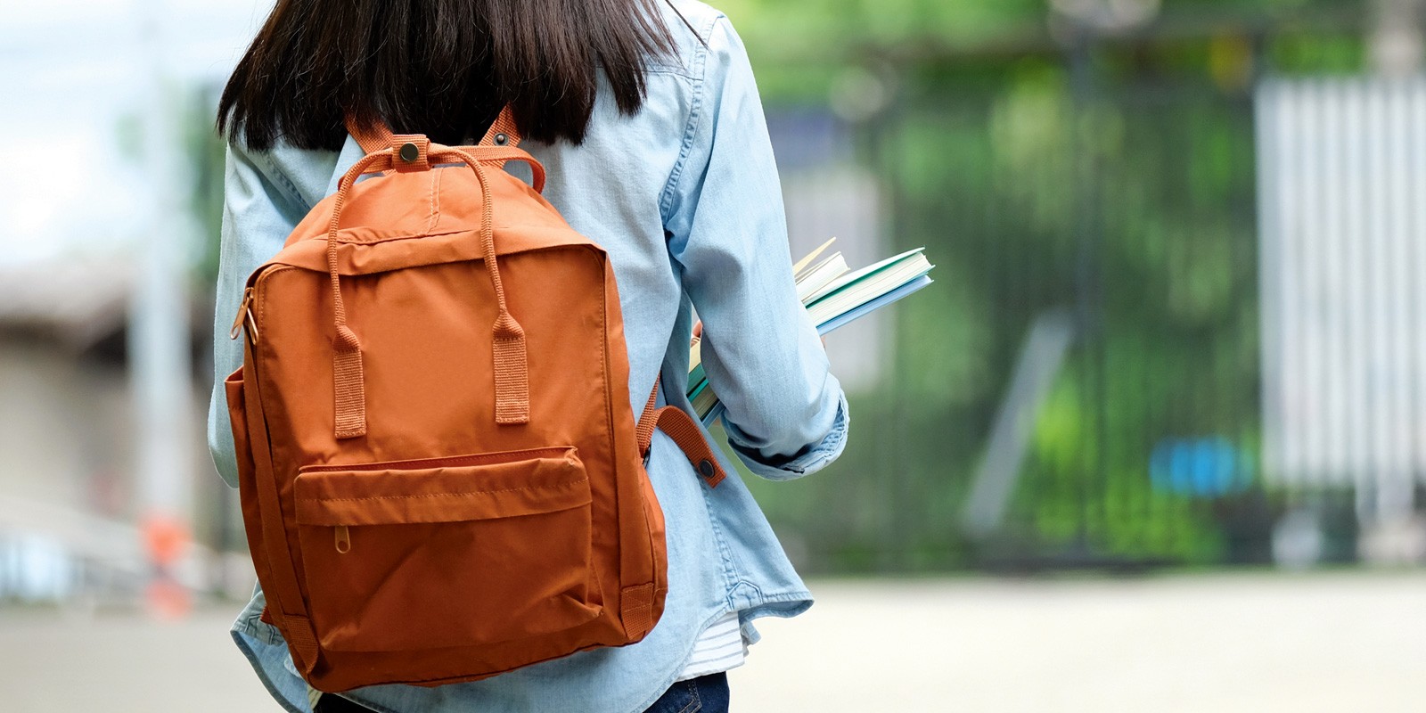 young female youth with backpack and books from behind