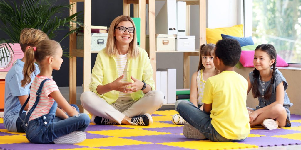 Adult sitting on the floor speaking a group of young children